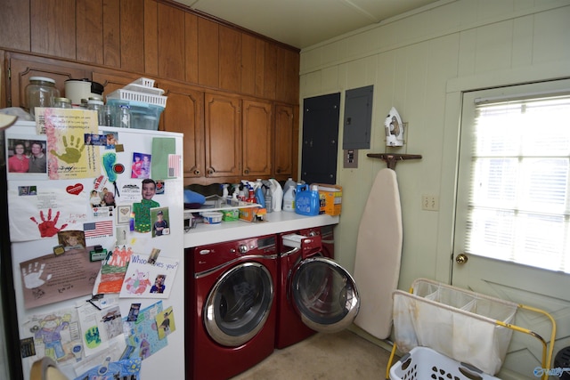 laundry room featuring washing machine and dryer, electric panel, cabinet space, and wooden walls