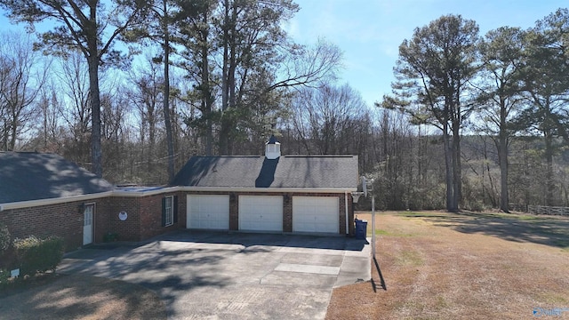 view of side of home with driveway, an attached garage, a chimney, and brick siding