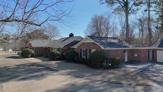 single story home featuring a garage, brick siding, driveway, and a chimney