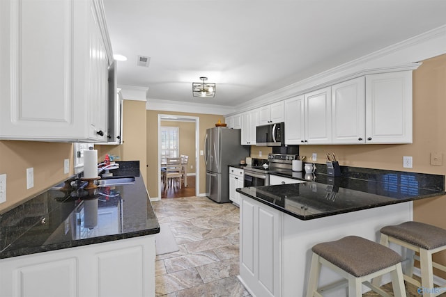 kitchen with visible vents, a kitchen bar, ornamental molding, a peninsula, and stainless steel appliances
