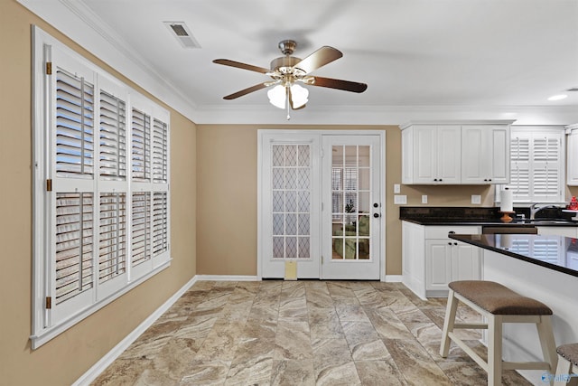 kitchen featuring dark countertops, visible vents, crown molding, white cabinetry, and a ceiling fan