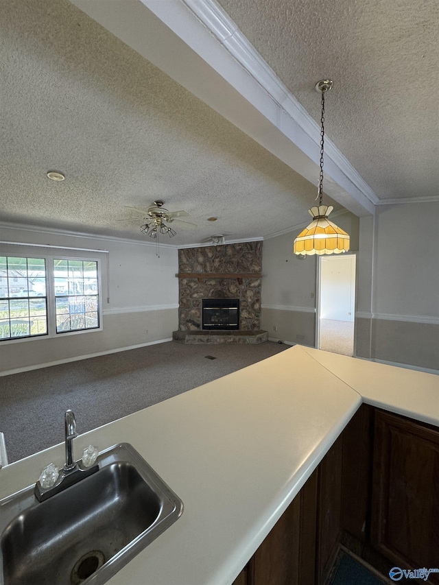 kitchen with carpet, a sink, a stone fireplace, pendant lighting, and crown molding