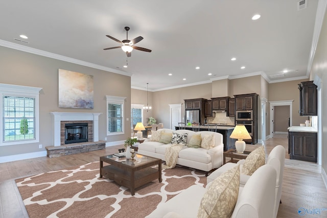 living room with ceiling fan, ornamental molding, a stone fireplace, and light hardwood / wood-style floors