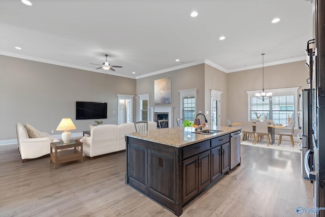 kitchen with a kitchen island with sink, ceiling fan with notable chandelier, sink, stainless steel dishwasher, and light hardwood / wood-style floors