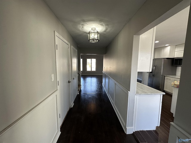 corridor featuring an inviting chandelier, a decorative wall, dark wood-style flooring, and a wainscoted wall