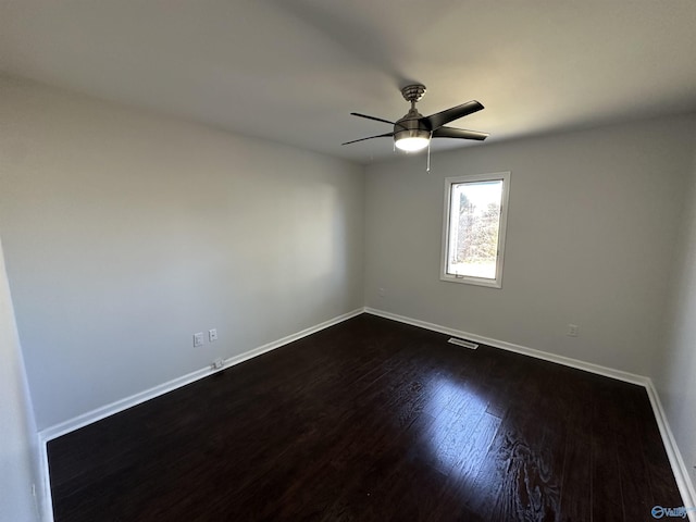 empty room with a ceiling fan, visible vents, dark wood finished floors, and baseboards