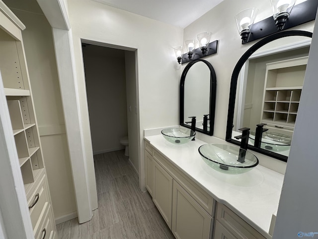 bathroom featuring toilet, double vanity, baseboards, and a sink