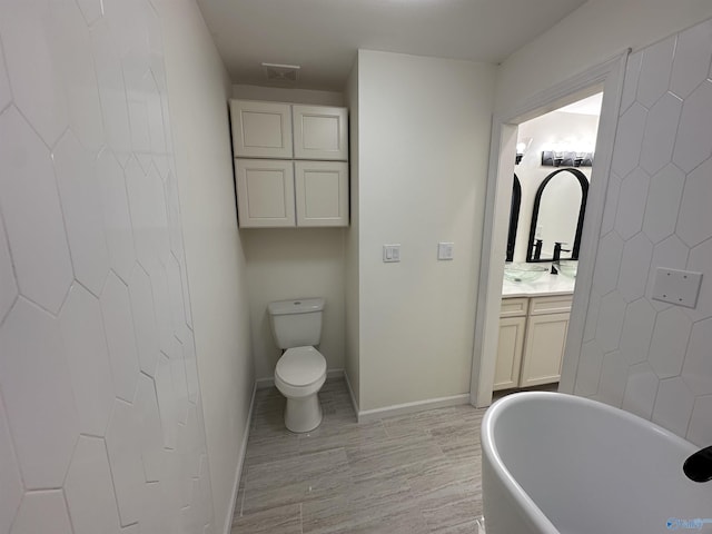 bathroom with baseboards, toilet, wood finished floors, a freestanding bath, and vanity