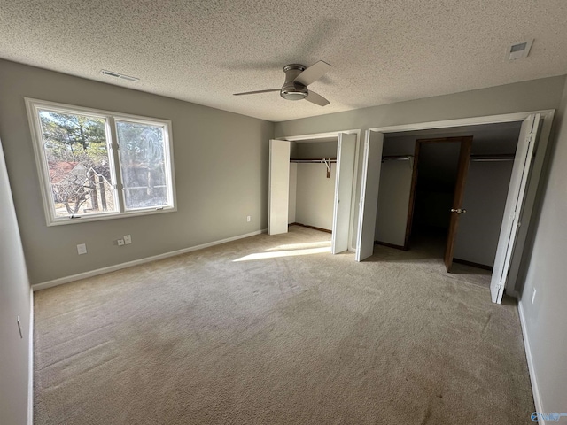 unfurnished bedroom featuring light carpet, two closets, visible vents, and baseboards