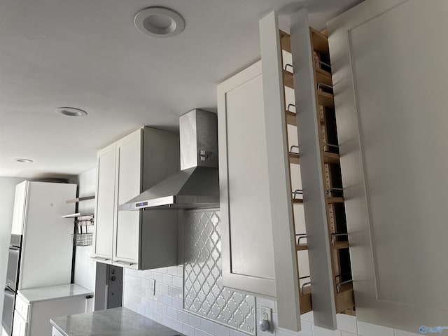 interior space featuring wall chimney range hood, tasteful backsplash, white cabinets, and freestanding refrigerator