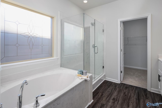 full bath featuring a garden tub, wood finished floors, vanity, a shower stall, and a walk in closet