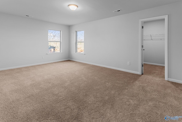 unfurnished bedroom with carpet floors, a walk in closet, a closet, visible vents, and baseboards