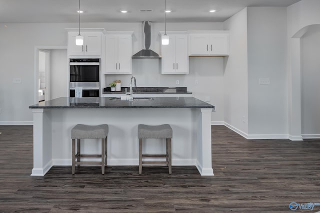 kitchen with white cabinets, stainless steel double oven, dark hardwood / wood-style flooring, and wall chimney exhaust hood