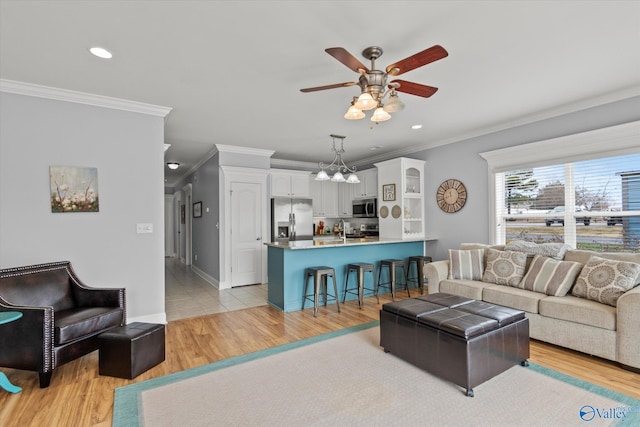 living room featuring ceiling fan with notable chandelier, ornamental molding, and light hardwood / wood-style floors