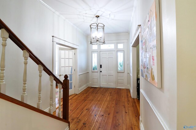 foyer featuring crown molding, stairs, wood-type flooring, and a notable chandelier