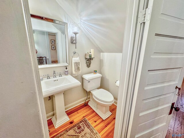bathroom with lofted ceiling, toilet, baseboards, a sink, and wood finished floors