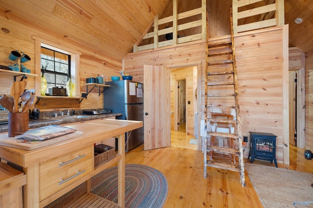 kitchen with light wood-type flooring, wood ceiling, sink, a wood stove, and stainless steel refrigerator