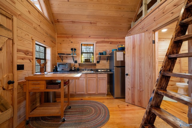 kitchen with vaulted ceiling, wooden walls, stainless steel refrigerator, and a healthy amount of sunlight