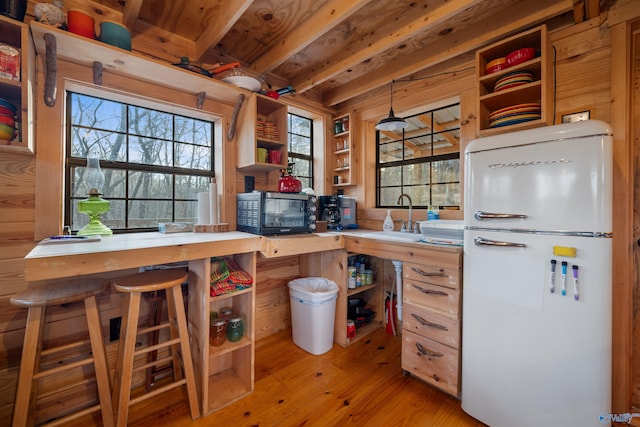 kitchen featuring beam ceiling, light hardwood / wood-style flooring, wooden counters, white refrigerator, and a breakfast bar area