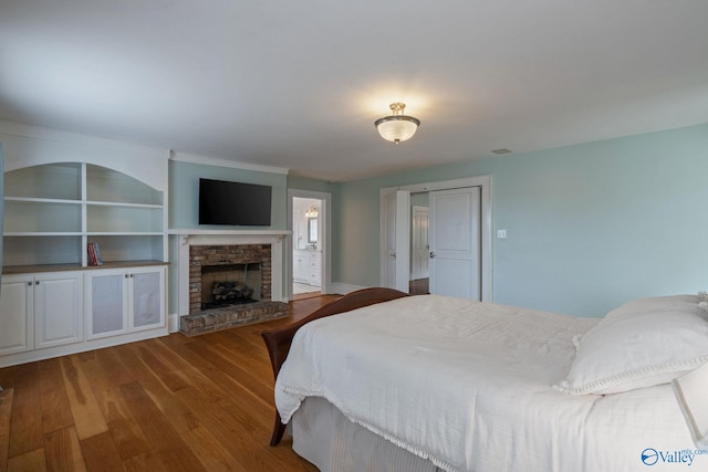 bedroom featuring connected bathroom, a brick fireplace, and light wood-type flooring