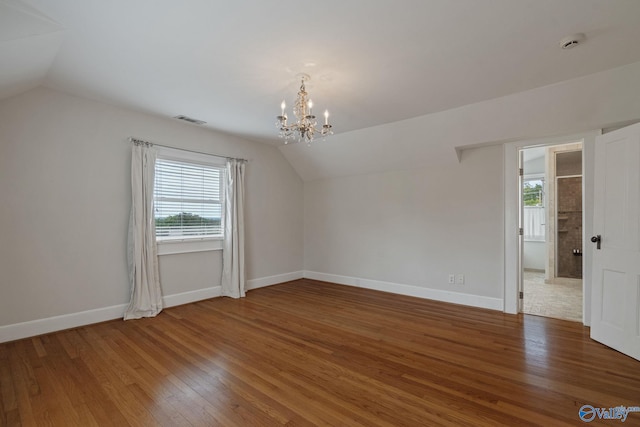 additional living space with hardwood / wood-style floors, vaulted ceiling, an inviting chandelier, and plenty of natural light