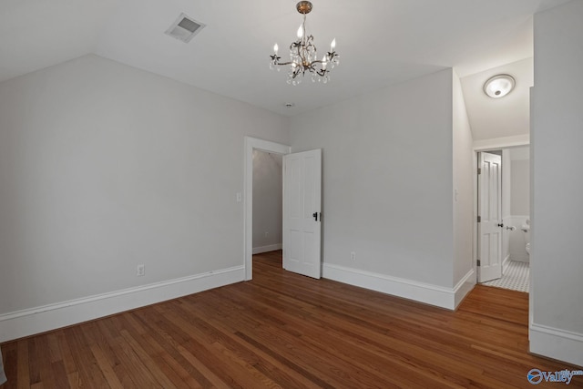 unfurnished bedroom featuring connected bathroom, an inviting chandelier, wood-type flooring, and vaulted ceiling