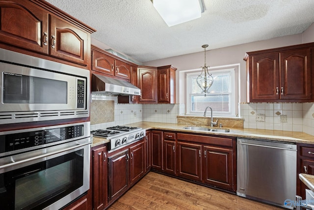 kitchen with tasteful backsplash, sink, appliances with stainless steel finishes, and wall chimney range hood