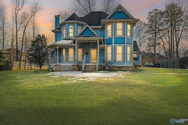 back house at dusk featuring a lawn and a porch