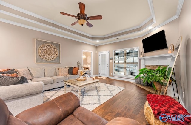 living area with crown molding, a fireplace, a raised ceiling, and wood-type flooring