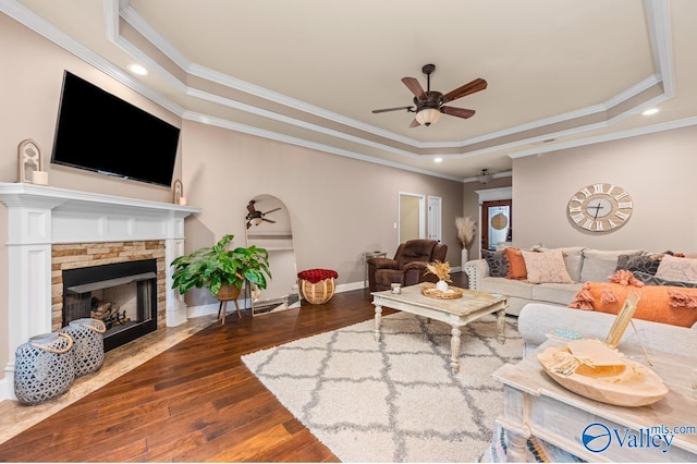 living room featuring dark wood finished floors, a stone fireplace, a ceiling fan, and a tray ceiling