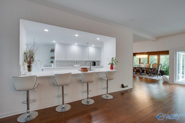 kitchen with kitchen peninsula, beam ceiling, a kitchen bar, and white cabinets