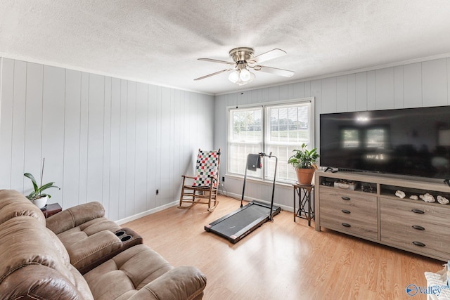 living room featuring wood walls, ceiling fan, a textured ceiling, and light hardwood / wood-style flooring