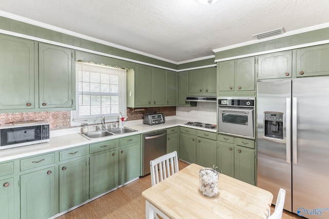 kitchen featuring appliances with stainless steel finishes, green cabinets, light hardwood / wood-style floors, crown molding, and sink