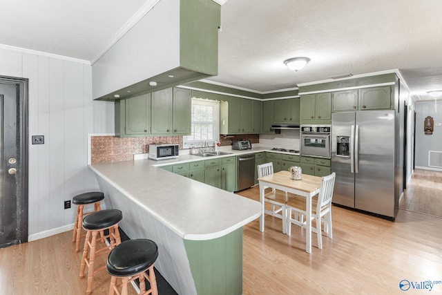 kitchen featuring light wood-type flooring, green cabinets, ornamental molding, stainless steel appliances, and kitchen peninsula