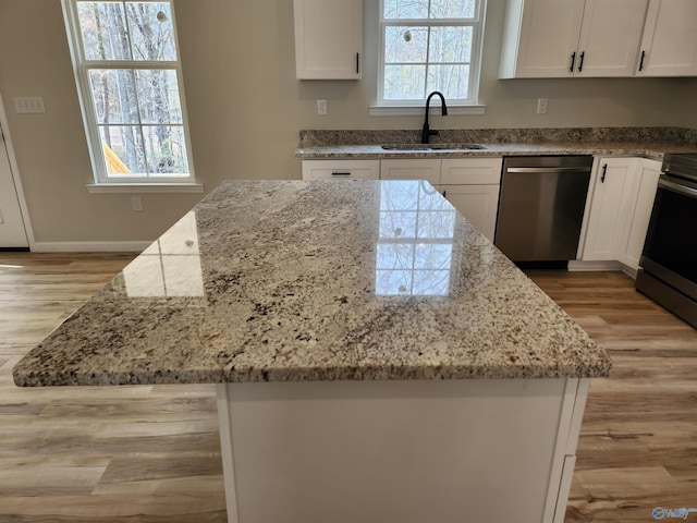 kitchen featuring stainless steel appliances, a sink, white cabinetry, and light stone countertops