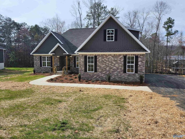 craftsman-style house with a shingled roof, brick siding, and a front lawn