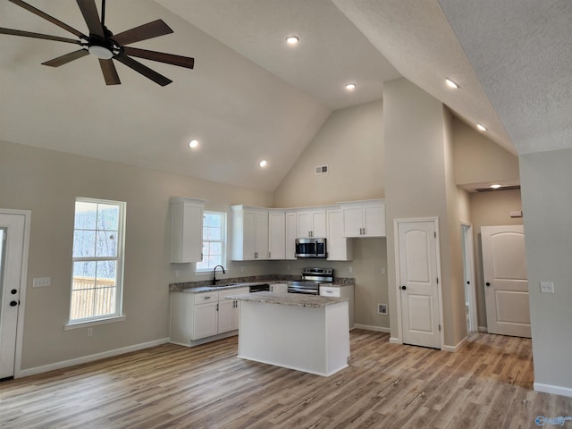 kitchen with a kitchen island, a sink, baseboards, white cabinets, and appliances with stainless steel finishes