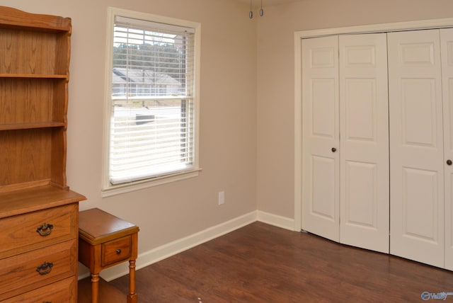 unfurnished bedroom with a closet, baseboards, and dark wood-type flooring