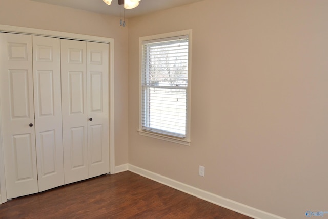 unfurnished bedroom with a closet, a ceiling fan, baseboards, and dark wood-style flooring