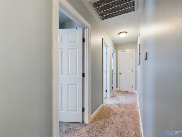 corridor with light colored carpet and a textured ceiling