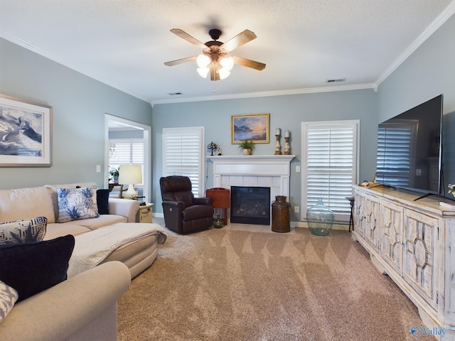 living room featuring a textured ceiling, a tiled fireplace, carpet floors, ornamental molding, and ceiling fan