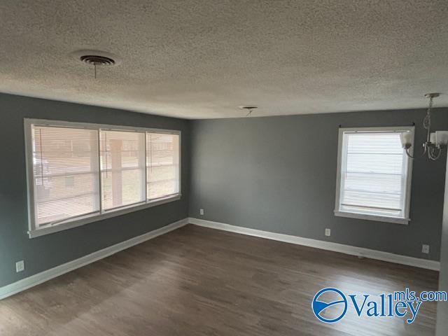 unfurnished room with plenty of natural light, dark hardwood / wood-style flooring, a textured ceiling, and a notable chandelier