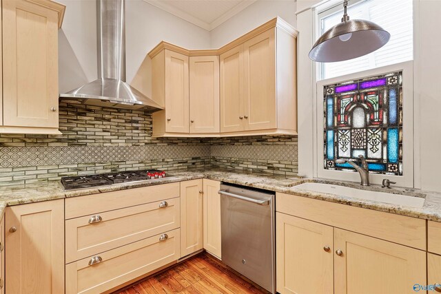 kitchen featuring wall chimney range hood, ornamental molding, sink, light hardwood / wood-style floors, and appliances with stainless steel finishes