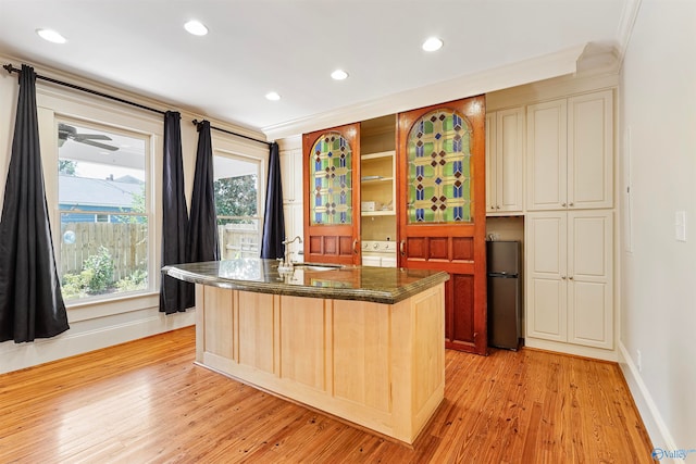 kitchen featuring stainless steel fridge, sink, light wood-type flooring, and a kitchen island with sink