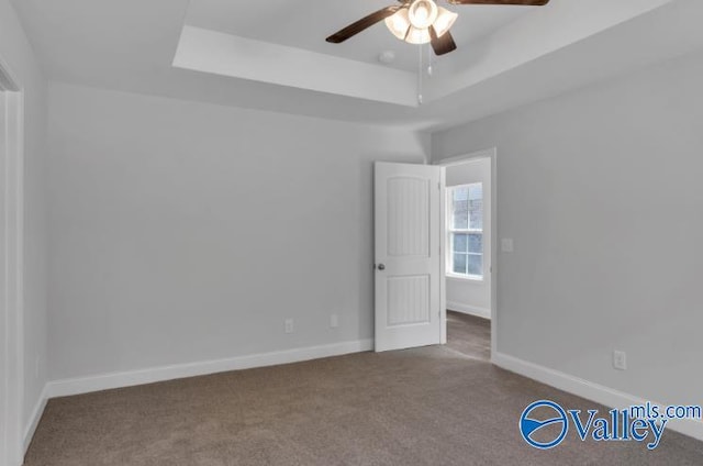 carpeted spare room with a raised ceiling and ceiling fan