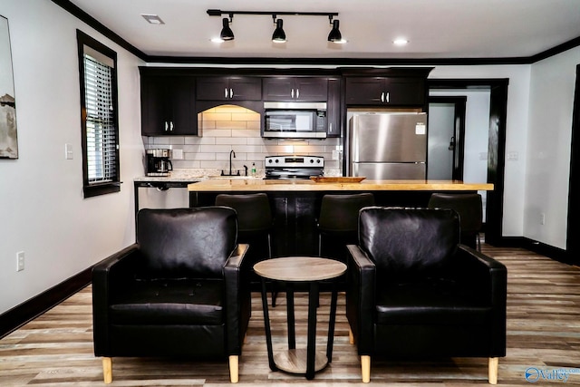 bar featuring light wood-type flooring, appliances with stainless steel finishes, crown molding, and decorative backsplash