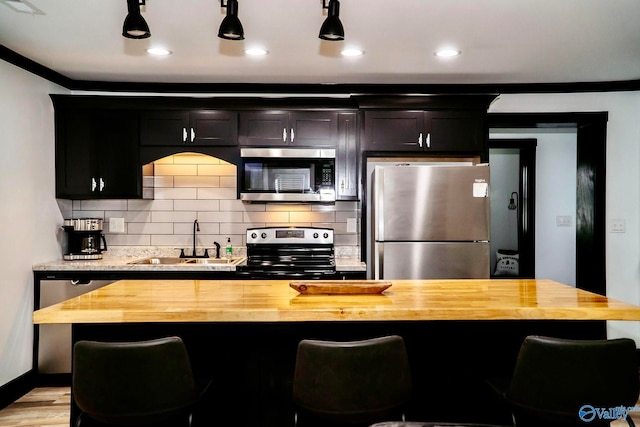 kitchen with a kitchen bar, stainless steel appliances, sink, and wooden counters