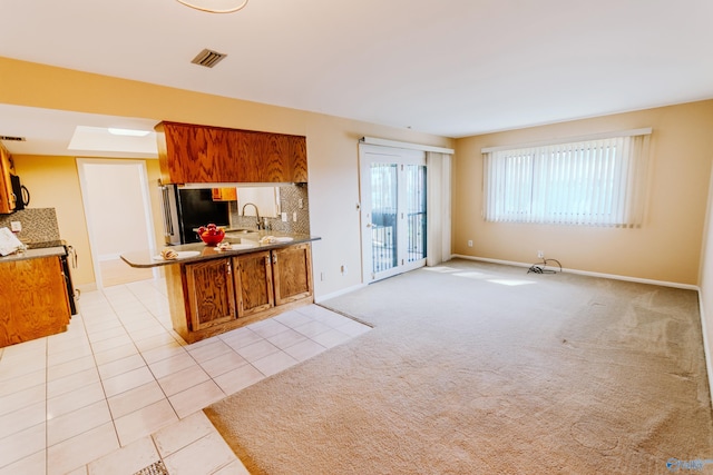 kitchen with refrigerator, a peninsula, brown cabinetry, and light colored carpet