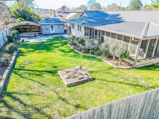 back of house with a fenced backyard, an outdoor structure, a sunroom, a yard, and a detached carport