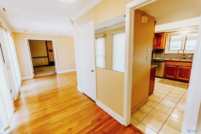 corridor featuring light wood-style floors, baseboards, ornamental molding, and a sink